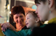 Adult and child taking part in a hands-on museum activity, gathered around an interactive display while exploring and learning together.